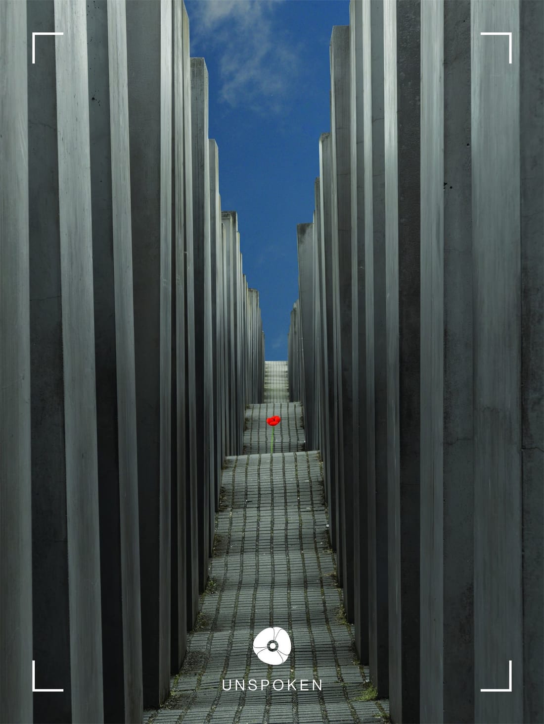 Print titled Unspoken: a narrow paved aisle between tall gray concrete stelae under a blue sky, with a single red flower on the path.