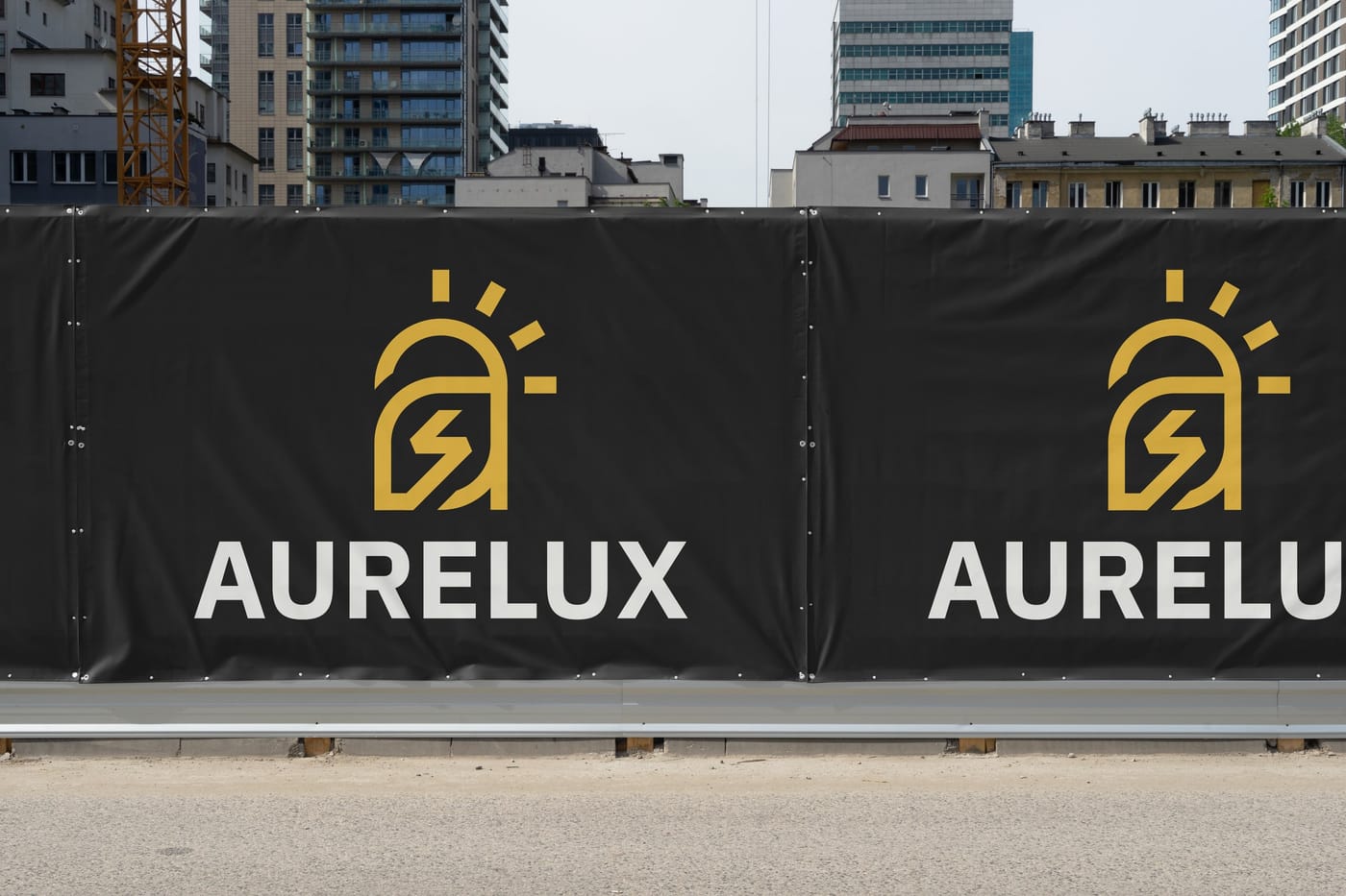 A construction-site fence wrapped in black Aurelux banners with the gold sun-and-bolt mark.
