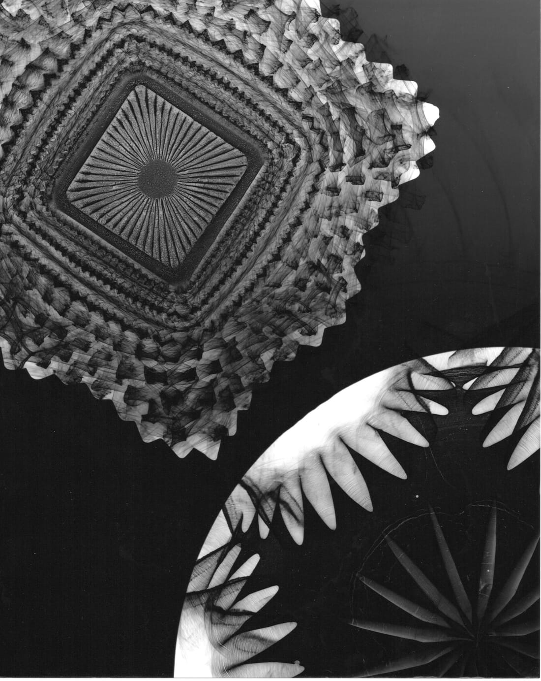 Photogram of cut-crystal dishes, their patterns glowing white against black.