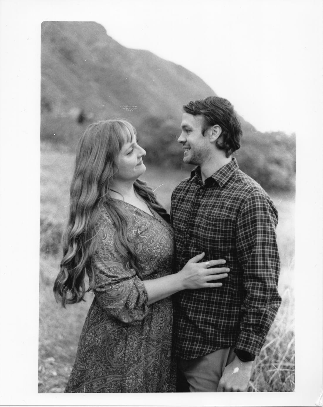 Print of a couple smiling at each other on a hillside below a mountain.