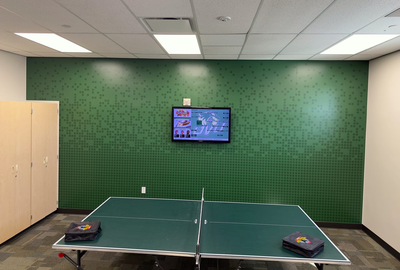 A break room with a full green pixel-pattern wall behind a ping-pong table.