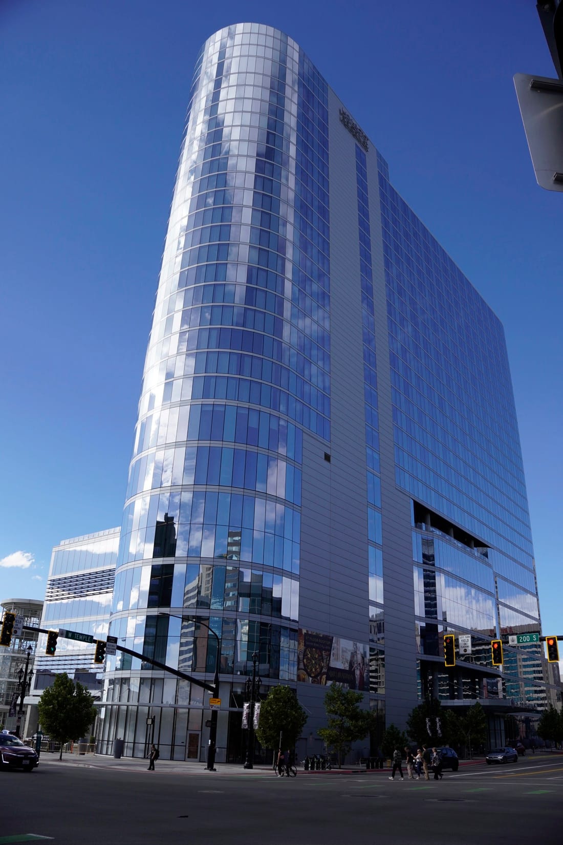 A curved glass tower reflecting the sky, looking up from a street corner with traffic lights.