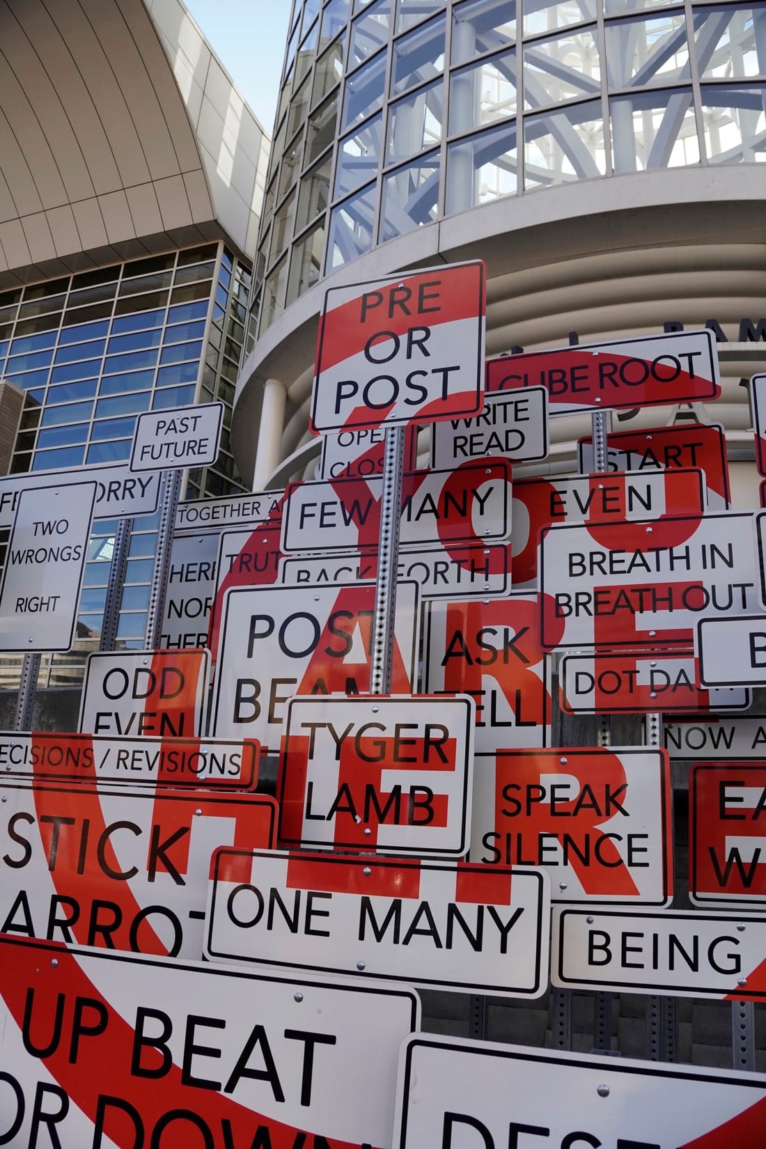 An art installation of white street signs printed with word pairs, in front of the convention center.