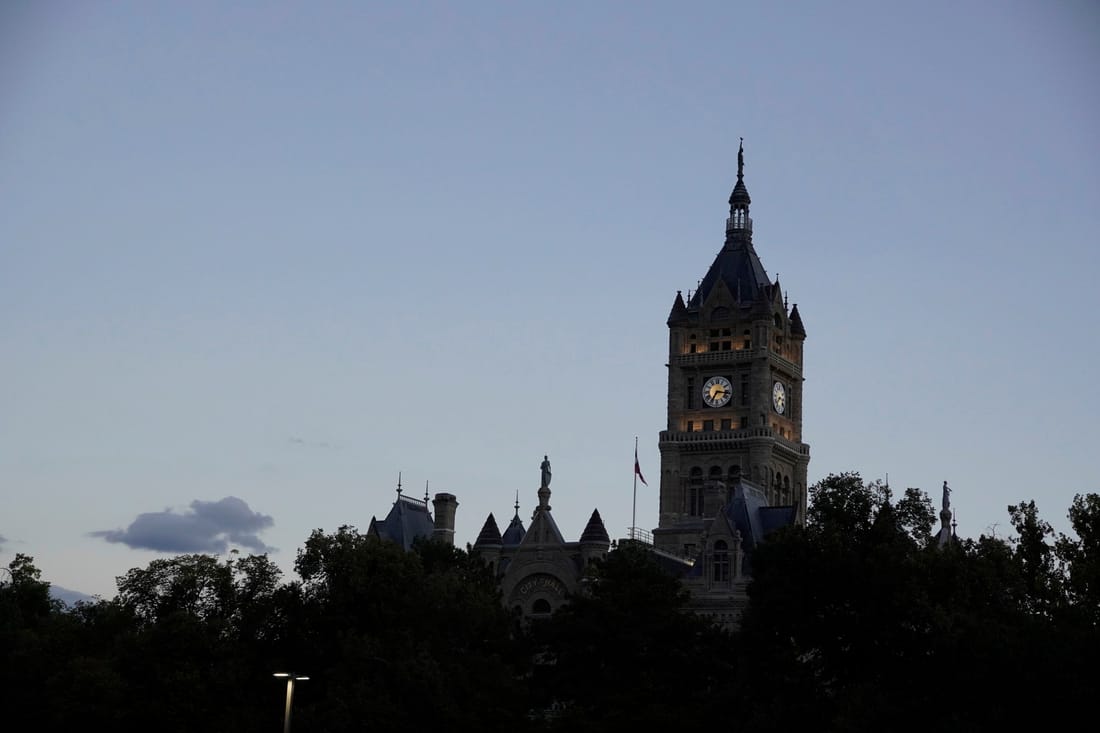 The Salt Lake City and County Building’s clock tower silhouetted above trees against a dusk sky.