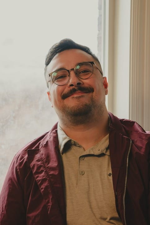 Ely smiling by a snowy window in a maroon jacket.