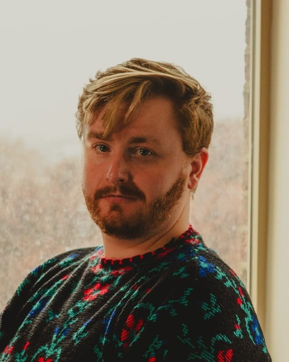 Paul Lingenbrink in a dark floral knit sweater by a snowy window, looking at the camera.