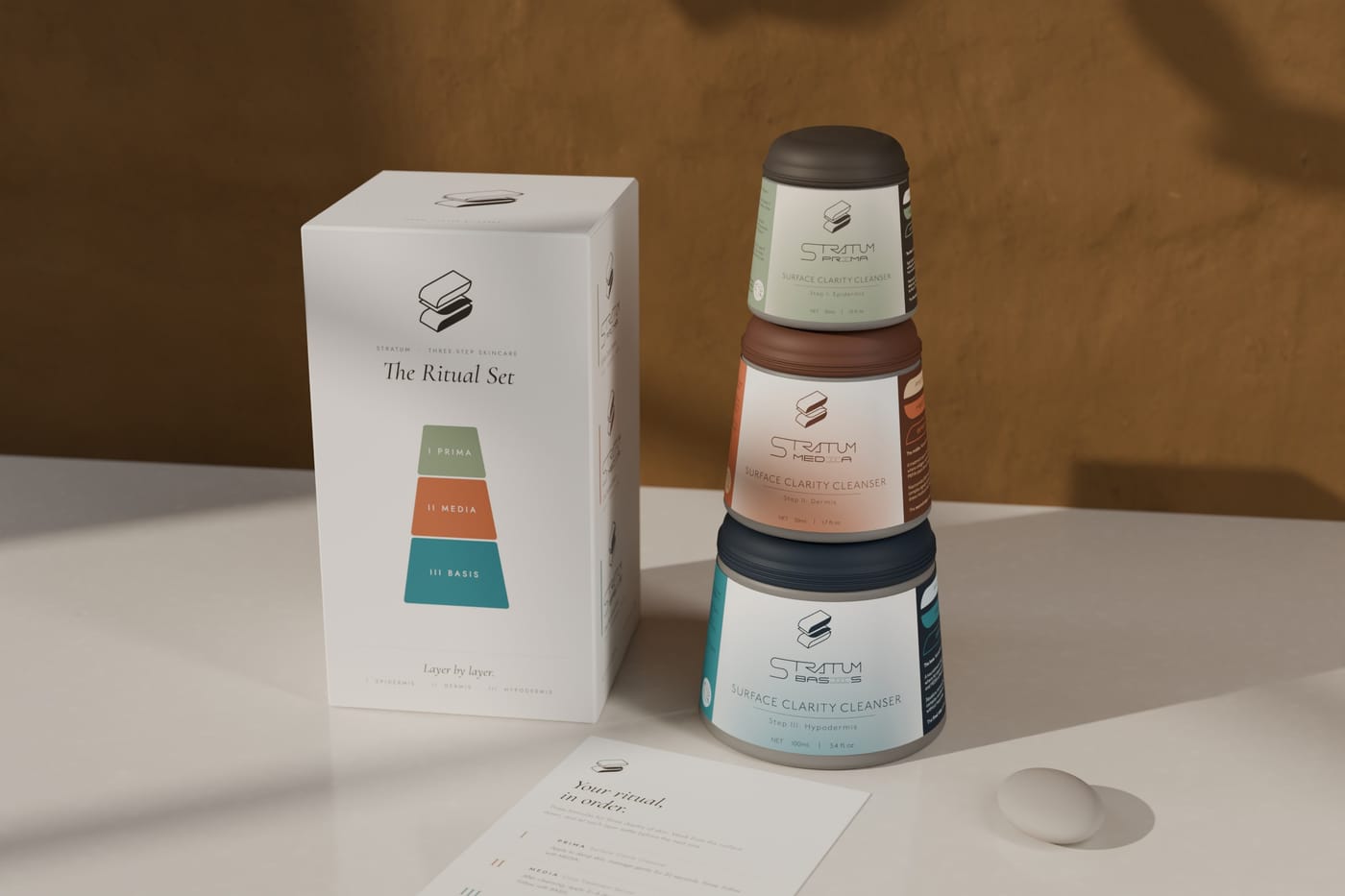 The Stratum Ritual Set on a pale stone table: a white carton whose front shows the three jars as a coloured cross-section of one cone, the three frosted-glass jars stacked beside it, and an insert card titled 'Your ritual, in order.'