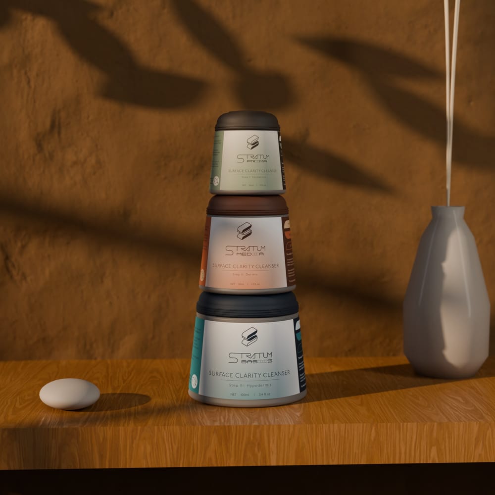 The Stratum Ritual Set on a pale stone table: a white carton whose front shows the three jars as a coloured cross-section of one cone, the three frosted-glass jars stacked beside it, and an insert card titled 'Your ritual, in order.'